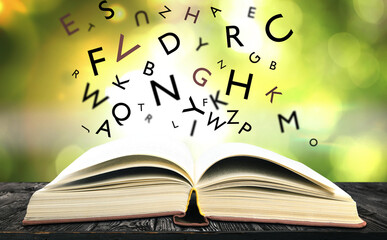 Open book with letters flying out of it on wooden table against blurred background