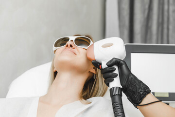 a young woman lies with her eyes closed and raises her hand up during the laser hair removal...