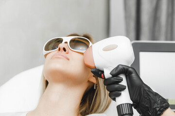 a young woman lies with her eyes closed and raises her hand up during the laser hair removal...