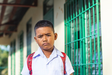 A young asian boy pouting while outside the classroom. Facial reaction after being scolded or...