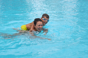 Vacation joy as mom and boy swim; true happiness. Reflects the growing trend of experiential family travel.