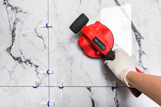 Tiler laying tiles using electric vibrating suction cup.