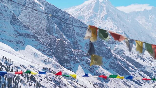 Defocused Buddhist Prayer flags waving in the wind in front of snow covered Himalayan mountains during the winter season at Keylong in Himachal Pradesh, India. Selective focus on the mountains.