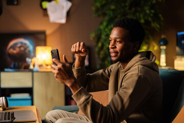 Attractive African American dark skinned social media content creator, using his phone to capture...