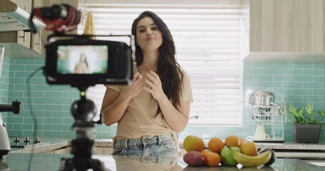 Woman, camera and live streaming in kitchen, broadcast and tutorial or teaching at home. Female influencer, webinar and vlogger or technology for video recording, jar and fruit for nutritional diet
