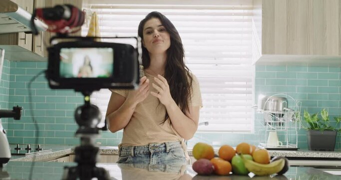 Woman, camera and live streaming in kitchen, broadcast and tutorial or teaching at home. Female influencer, webinar and vlogger or technology for video recording, jar and fruit for nutritional diet
