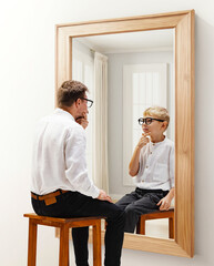 Man in formal wear sitting and looking in mirror with reflection of him being a child. Dreams and...