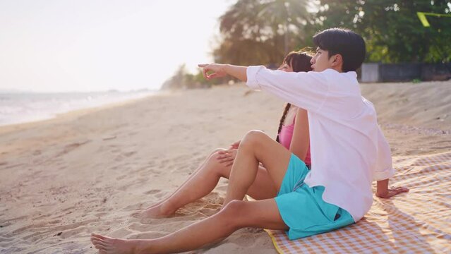 Asian young couple having picnic on the beach during summer together. 