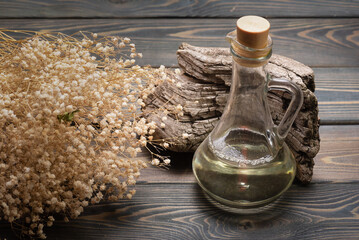 Natural oil in the bottle and dried gypsophila on the wooden table background close up.