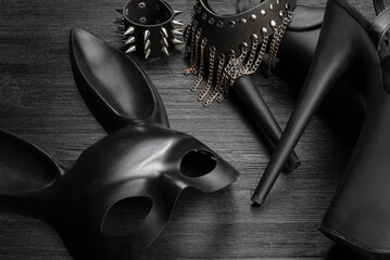 Black rabbit mask, studded leather bracelets, high heels shoes and neck choker on the black wooden...