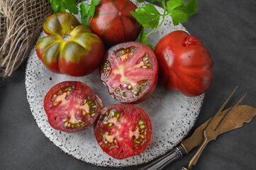 Fresh red ripe tomatoes on wooden cutting board with parsley, dark rustic background. Cut tomatoes...