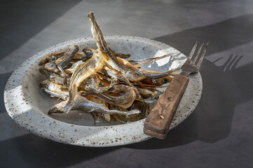 Dried salted sprat smelt. Baltic dried smelt fish on a handmade round clay plate, an appetizer for...