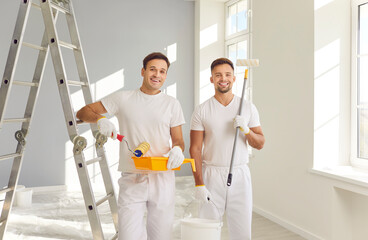 Portrait of smiling happy team of house painters looking at camera holding paint rollers and going...