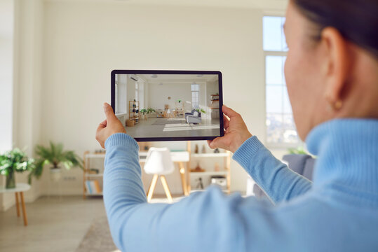 Woman takes photograph of large renovated home interior. Property owner or estate agent uses wide angle camera on smart tablet to take photo or give walkthrough video tour about new apartment for sale