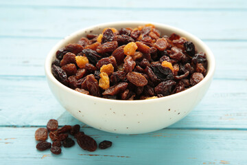 Raisins in white bowl on blue wooden background.
