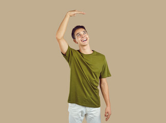 Portrait of young smiling happy boy wearing green casual t-shirt want to grow up showing height...