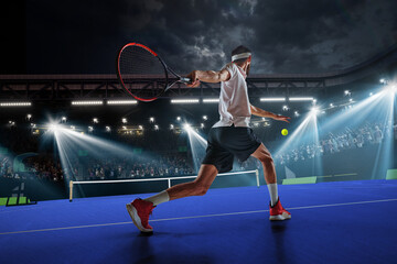 Dynamic image of young man, tennis player in motion during game, hitting ball with racket. Tennis court and fan zone. Concept of sport, competition, tournament, action, success