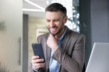 Joyful smiling satisfied businessman typing text message on phone, man in business suit browsing...