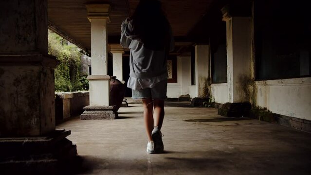 a girl walking through an abandoned building, back view