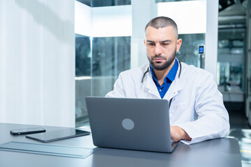 Fototapeta premium Professional male doctor focuses on providing patient care while using laptop in modern medical office setting, highlighting dedication and expertise in healthcare.