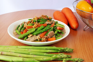 Stir-fried asparagus with pork and carrots on a wooden table

