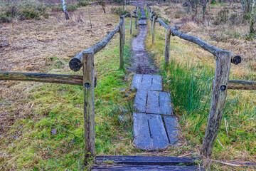 Top angle perspective of a pedestrian path between wooden fences on plain with muddy terrain fading...