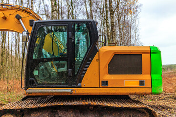 Closeup of cab of a grab excavator with bare trees in background with a cloudy sky, construction of rural roads in a forest area