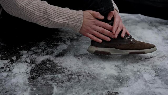 Man sitting on ice grabs injured ankle, examines cut on hand after slipping
