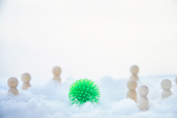 A green ball with appendages similar to the coronavirus, wooden men around and snow. COVID-19 disease is more common in winter in the cold
