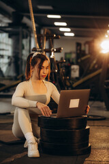 A woman communicates with a trainer through a laptop and works out in the gym