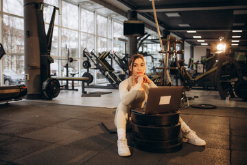 A woman with a laptop sits in the gym. Online training