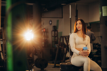 Fototapeta na wymiar caucasian woman in sportswear sitting on floor near dumbells rack resting and rekaxing after having excercise and workout in gym