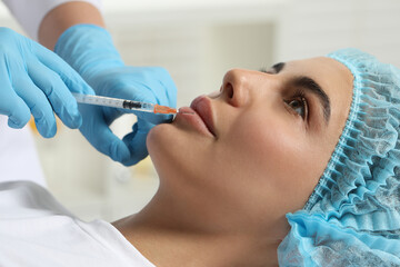 Doctor giving lips injection to young woman in clinic, closeup. Cosmetic surgery