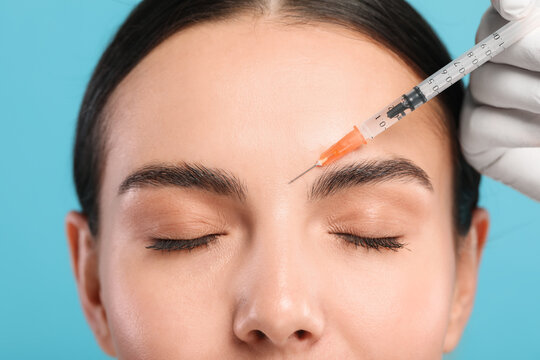 Doctor giving facial injection to young woman on light blue background, closeup. Cosmetic surgery