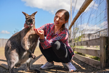 Young woman posing with kangaroo, feeding the animal some fruit from her hand