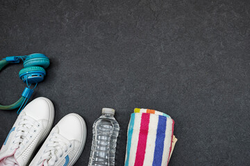 Healthy lifestyle, sport or athlete's equipment set : bottle of water with blue wireless headphone and towel, sneakers on gray background