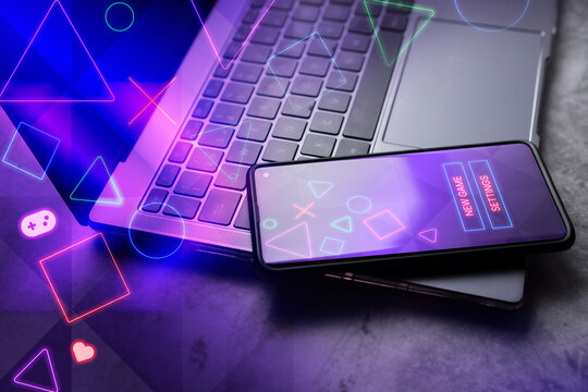 Smartphone laying on laptop with gaming interface on screen. Playing online concept with empty space for text. Online entertainment and gamification.