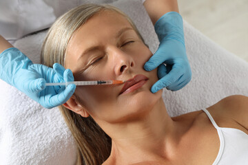 Doctor giving lips injection to senior woman in clinic. Cosmetic surgery
