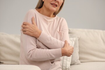 Mature woman suffering from pain in arm indoors, closeup. Rheumatism symptom