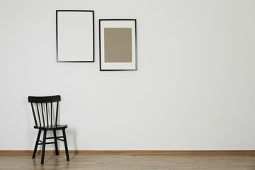 Black chair and frames in room with white wall, space for text. Interior design