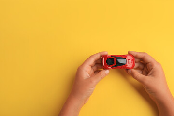 Child holding toy car on yellow background, top view. Space for text