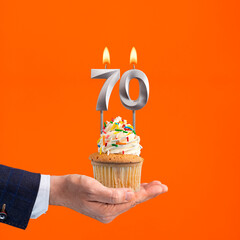 Hand holding birthday cupcake with number 70 candle - background orange