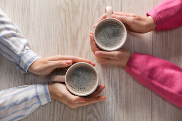 Women with cups of hot coffee at light wooden table, top view