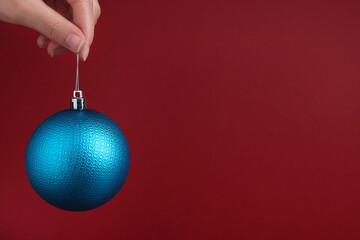 Woman holding blue Christmas ball on red background, closeup. Space for text