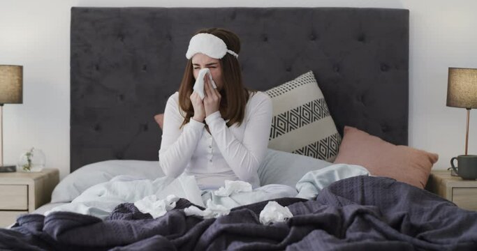 Sick, sneezing and woman blowing nose in bed a with tissue, allergies or viral infection at home. Flu, cough and female person in a bedroom with toilet paper, bacteria or tuberculosis risk in a house