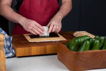 Close up of sushi chef hands preparing Japanese food. Man cooking sushi at restaurant or at home. Portion of Traditional Asian rice on nori seaweed.