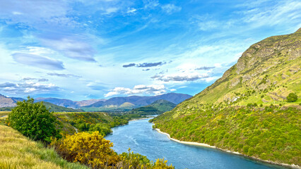River in between mountains summer day New Zealand - blue sky with slights clouds - green mountains traversed by a river on beautiful sky - Powered by Adobe