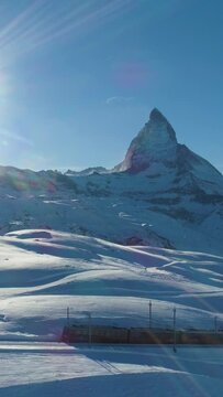 Matterhorn Mountain and Cog Railway Train in Sunny Winter Day. Swiss Alps. Switzerland. Aerial View. Drone Flies Sideways. Vertical Video