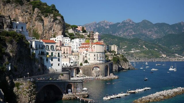 Collegiate Santa Maria Maddalena church and moored boats in harbor of port Atrani. Mediterranean seascape and boats. Beautiful Italian beach and coastline shot on sunny summer day, slow motion.