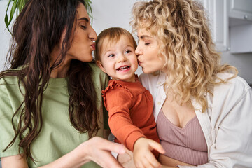 loving cheerful lesbian couple in homewear posing happily with their baby girl, modern parenting